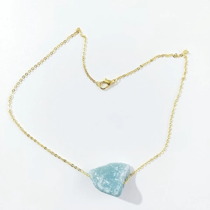 Detail of a light blue raw crystal stone pendant on a delicate gold link chain