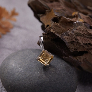 Macro view of a square-cut yellow gemstone pendant on a natural stone background