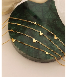 Detailed view of delicate gold-plated heart pendant necklaces on dark green marble surface