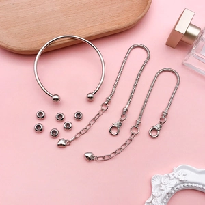 Flat lay of silver DIY jewelry set with open bangle, heart charm bracelets and beads