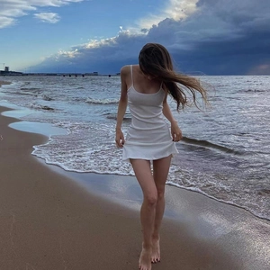 Close-up of white bodycon camisole dress worn on a beach with ocean waves background