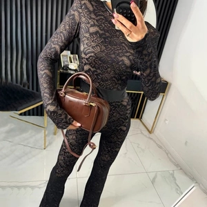 Detail view of stylish black lace long sleeve jumpsuit with flared trousers and chic handbag