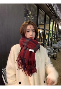 Close-up of red plaid scarf with fringe detail and a stitched label on soft fabric