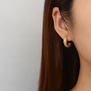 Detailed close-up of a gold-tone C-shaped earring with woven texture and small rhinestones