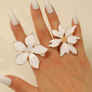 Détail de grandes bagues fleurs en émail blanc aux bords dorés et centre perlé portées