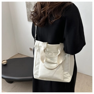 Detailed view of a white nylon tote bag with a front flap pocket and dual straps