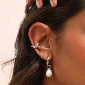 Detail view of stacked silver wave earrings with micro-inlaid diamonds and irregular pearl
