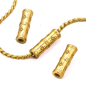 Macro shot of gold cylinder beads with sunburst engraving on a twisted chain link