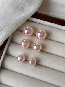 Three pairs of pink iridescent pearl studs in varied sizes displayed on silk fabric