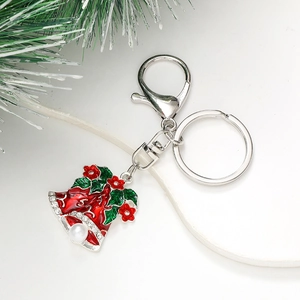 Macro detail of Christmas bell keychain with red enamel, holly leaves and pearl dinger