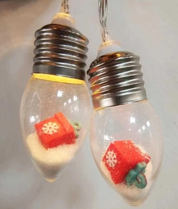 Close-up of LED Christmas bulb ornaments with miniature snow scene and red gift box