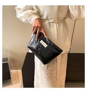 Close-up of black glossy cosmetic bag with fine pleated texture and fashion label