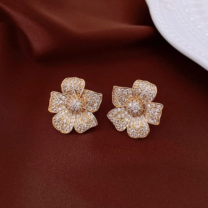 Detailed macro view of golden flower earrings with sparkling pavé-set zircons on dark fabric
