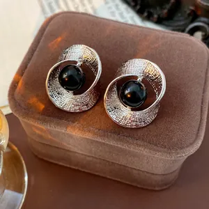 Elegant twisted silver hoop earrings with a central black bead on a velvet jewelry box