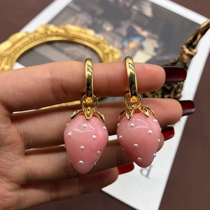 Close-up of pink strawberry pearl earrings with gold leaf detail and french hooks