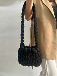 Detailed close-up of a handmade chunky knit shoulder bag in black on a beige suit model