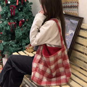 Close-up of a large red checkered tweed tote bag worn by a model in a cozy winter setting
