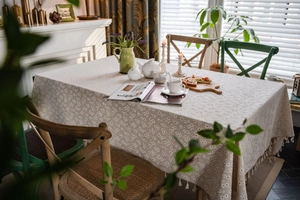 Detailed view of beige cotton linen tablecloth with white daisy prints and fringe edges