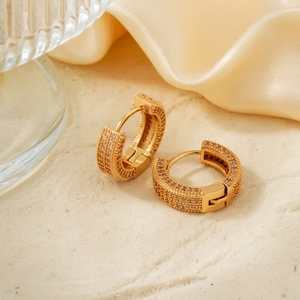 Golden hoop earrings with micro-pave zircons and belt buckle design on silk background