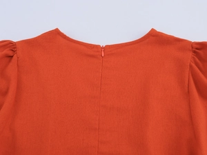 Close-up of orange-red V-neck dress back featuring invisible zipper and pleated puff sleeves