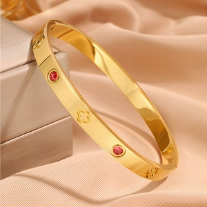 Macro shot of gold-plated clover bracelet with red zircon inlay on silk background