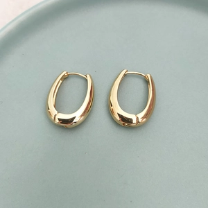 Detailed top view of gold-tone U-shaped oval hoop earrings on a ceramic dish