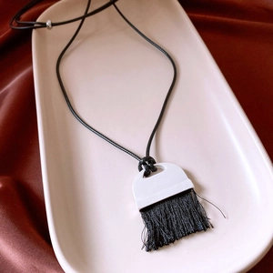Detail view of a vintage leather tassel necklace with a white geometric pendant on silk
