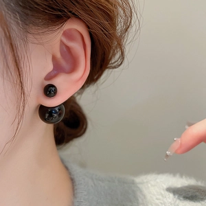 Detailed close-up of classic black double-beaded stud earrings on model ear