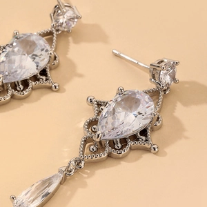 Macro detail of pear-cut zircon earrings with intricate silver baroque metalwork