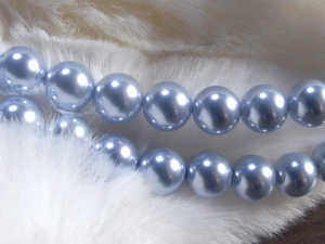 Macro detail of high-gloss light blue round pearls on soft white faux fur background