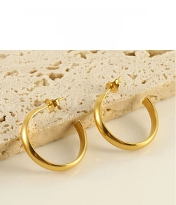 Detail of matte gold C-shaped earrings with a textured surface on minimalist stone