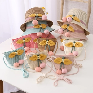 Detail of children's summer straw hat and matching crossbody bag with cherry pom-poms