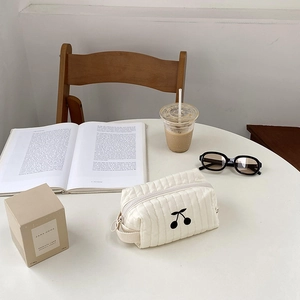 Quilted cherry cosmetic bag shown on a coffee table with books and accessories