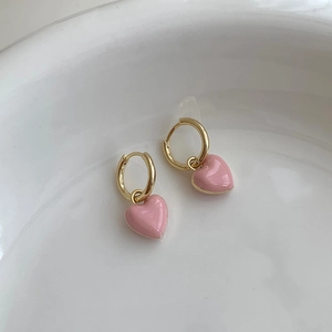 Close-up of sweet pink heart earrings with gold hoops on a white ceramic tray