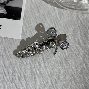 Macro shot of silver metal bow hair clip with sparkling rhinestones on white surface