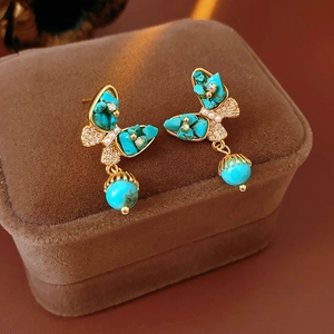 Gros plan détaillé de boucles d'oreilles papillon dorées avec turquoise sur velours brun