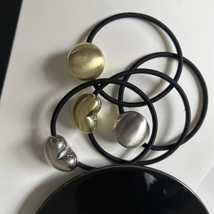 Close-up of black elastic hair ties with brushed gold and silver heart-shaped charms