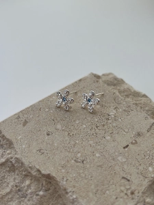 Macro detail of silver floral stud earrings with blue gemstone on textured stone