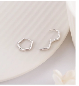 Detailed macro view of silver flower scalloped edge earrings on white ceramic tray
