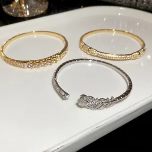 Minimalist gold plated zircon bangles with geometric and feather designs on ceramic tray