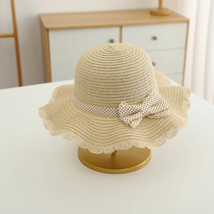Close-up of beige straw sun hat featuring wavy lace edges and polka dot ribbon bow