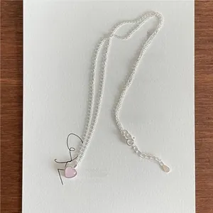 Close-up of S925 sterling silver chain with a pink heart pendant on wooden surface