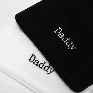 Close-up of black and white knitted beanies with Daddy embroidery and fine texture