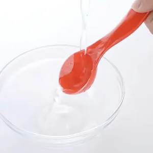 Red plastic measuring spoon being rinsed under water, featuring an easy-to-clean design