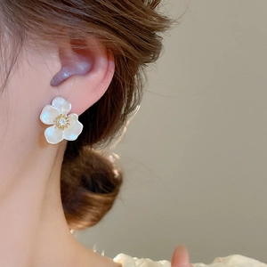 Close-up of elegant white flower stud earrings with gold accents and zircon on model's ear