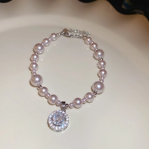 Detail of light pink pearl bracelet with zircon paved sphere pendant on ceramic dish