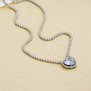 Detail of a tennis chain necklace featuring a large heart-shaped blue gemstone pendant