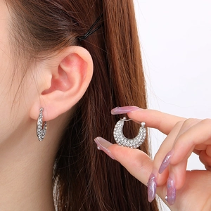 Polished silver U-shaped earrings with white zircons shown on model and held by hand