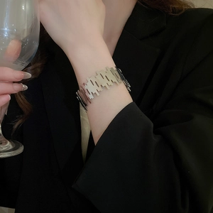 Detail shot of a silver geometric cut-out wide cuff bracelet on a model wearing black suit