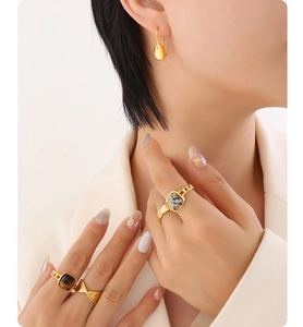 Detail of gold water drop earrings and gemstone rings worn by a model in elegant style